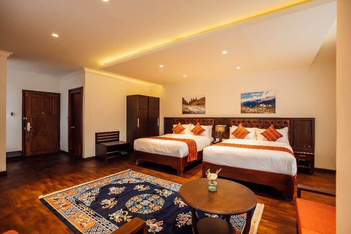 A hotel room with two beds, a wooden floor, a round table, and a decorative rug.