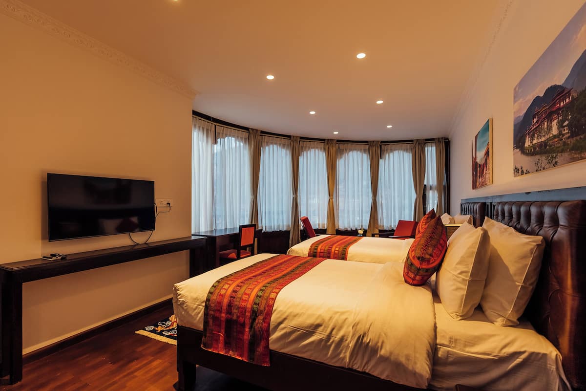 A hotel room with two beds, a flat-screen TV, a desk, and a large window with curtains.