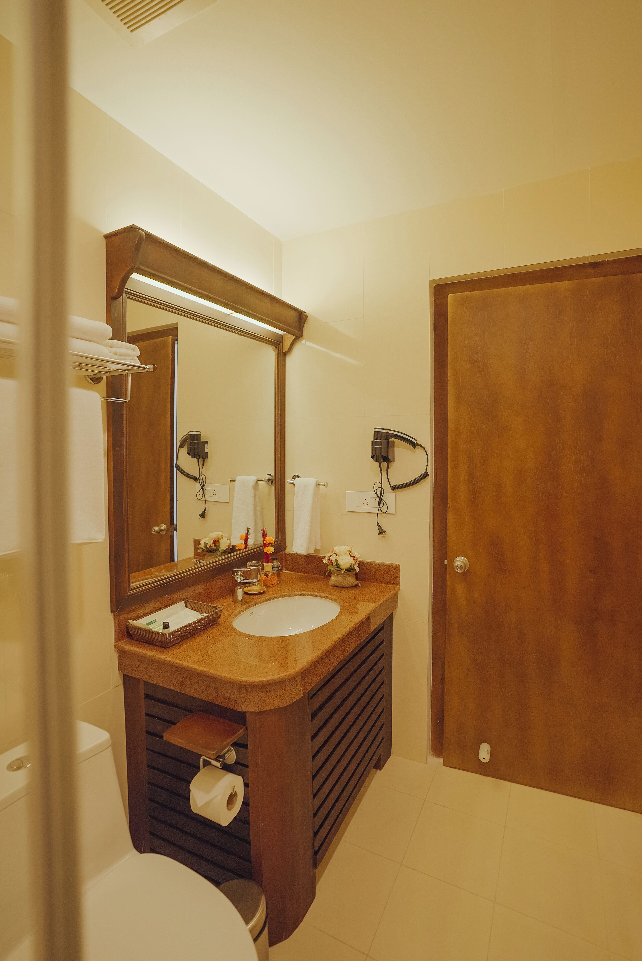A bathroom with a wooden vanity, a large mirror, a toilet, and a door.