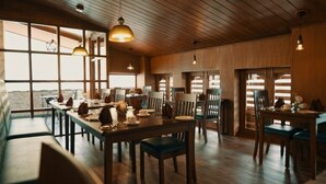 A dining area with wooden tables and chairs, large windows, and hanging pendant lights. - Lhaki Hotel Thimphu (Thimphu)