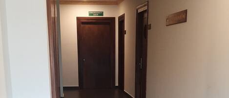 Un pasillo largo y estrecho con suelo de baldosas oscuras, una puerta de madera al final y un techo con un diseño decorativo.