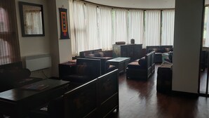 Ein Wohnzimmer mit einer Sofagarnitur, einem Couchtisch und einem Fernseher. Es gibt ein Fenster mit Vorhängen, eine Heizung und einen Bilderrahmen an der Wand.