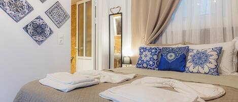 A neatly made bed with folded towels, a bedside table with a lamp, and decorative wall tiles.