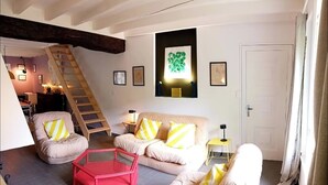 Una sala de estar con una escalera, dos sofás, un sillón rojo y una lámpara amarilla.