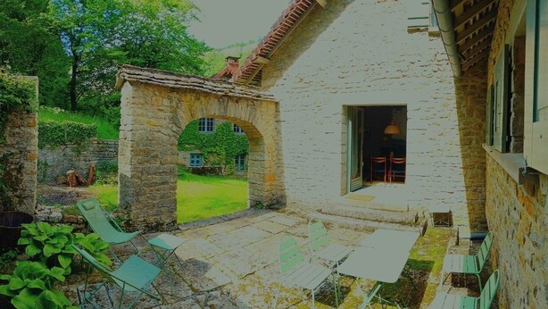 Un edificio de piedra con un arco que da a un patio interior. Hay zonas de estar al aire libre con sillas y mesas.
