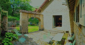 Un edificio de piedra con un arco que da a un patio interior. Hay zonas de estar al aire libre con sillas y mesas.