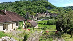 Una casa de piedra con techo inclinado, un pequeño jardín y vistas a un pueblo con edificios tradicionales y una iglesia.