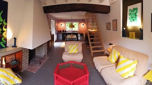 Una sala de estar acogedora con chimenea, una escalera y una cocina al fondo.