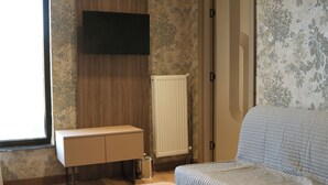 A room with a bed, a small table, a TV mounted on the wall, a radiator, and a cabinet. - Arun Suites (Gaziantep)