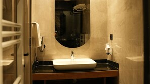 A modern bathroom with a large oval mirror, a white sink, and a towel rack. - Arun Suites (Gaziantep)