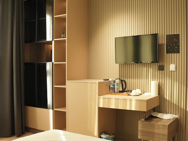 Habitación de hotel con televisión montada en la pared, minibar, escritorio pequeño con lavabo y un cubo de basura.