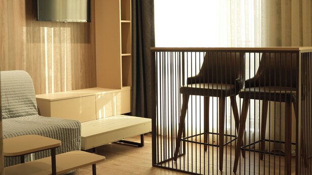 A modern room with a sofa, a small table, a TV mounted on the wall, and a window with curtains. - Arun Suites (Gaziantep)