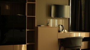 A modern hotel room with a bed, a desk with a lamp, a chair, and a wardrobe. - Arun Suites (Gaziantep)