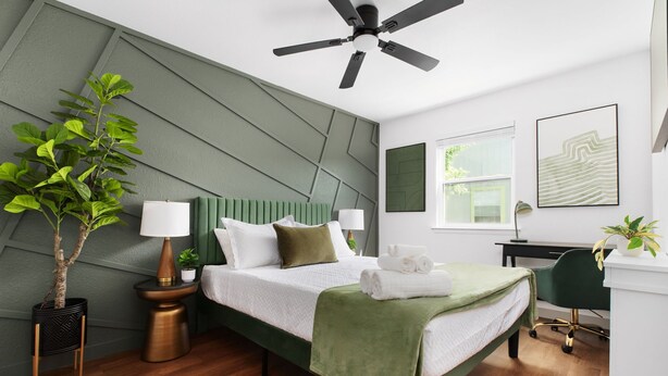 A modern bedroom with a green bed, a ceiling fan, a desk, and a potted plant. - Stylish 2BR Oasis with Private Patio - Sleeps 8 (Austin)