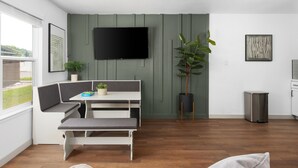 A modern living room with a white bench, a table with a plant, a TV mounted on the wall, and a trash bin. - Chic 2BR Escape Sleeps 8  w Private Patio (Austin)