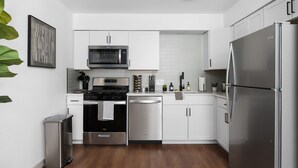 A modern kitchen with white cabinets, stainless steel appliances, and a wooden floor. - Chic 2BR Escape Sleeps 8  w Private Patio (Austin)