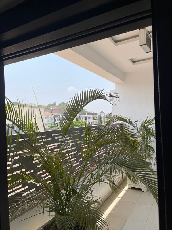 A balcony with a view of buildings, a tiled floor, and a palm plant. - UrbanEdge Hotel (Abuja)