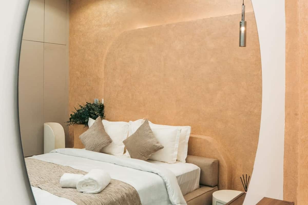 A modern bedroom with a bed, bedside table, and a unique circular mirror.