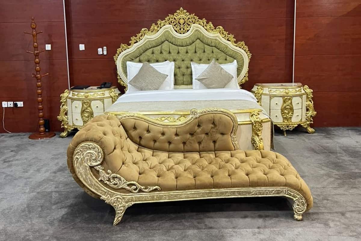 A large, ornate bed with a tufted headboard and gold detailing, flanked by matching nightstands.