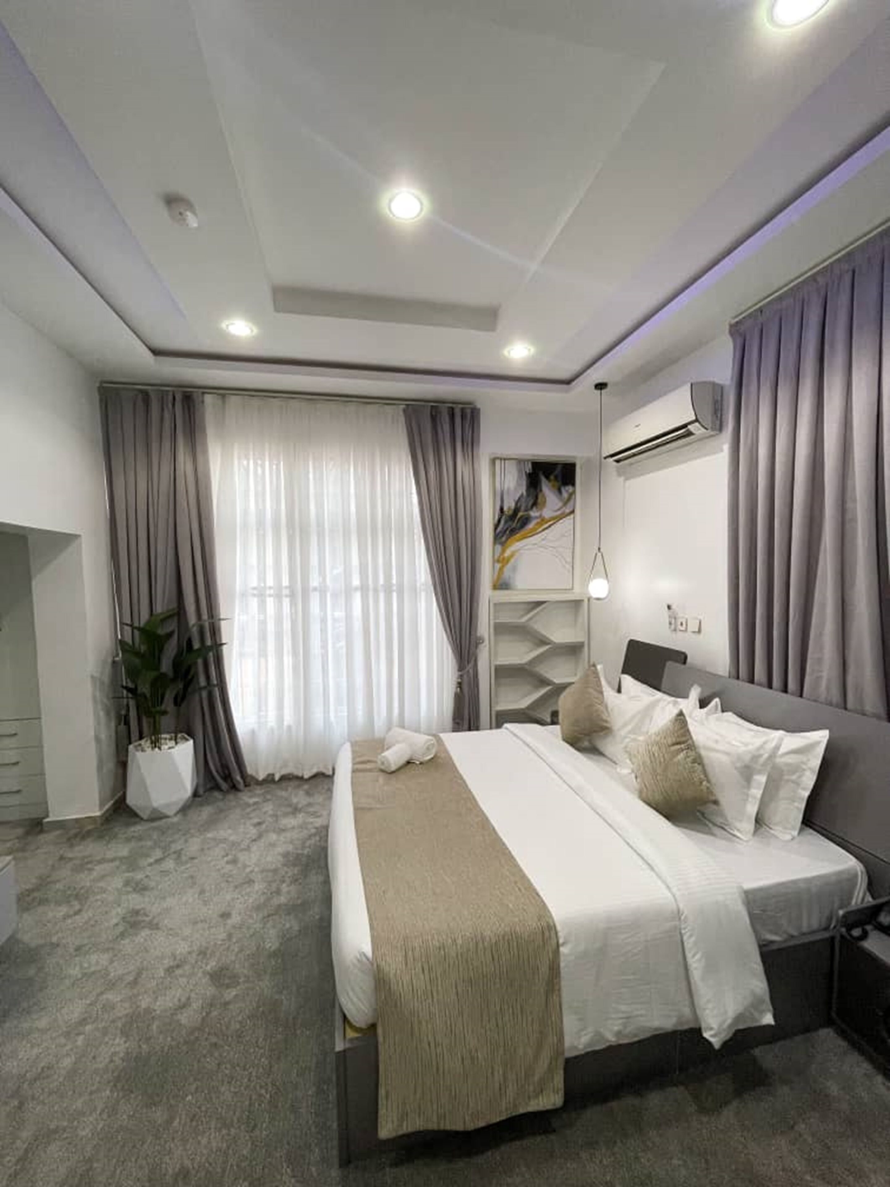 A modern bedroom with a bed, a potted plant, and a large window with curtains.