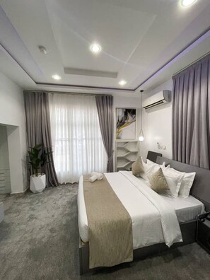 A modern bedroom with a bed, a potted plant, and a large window with curtains. - UrbanEdge Hotel (Abuja)