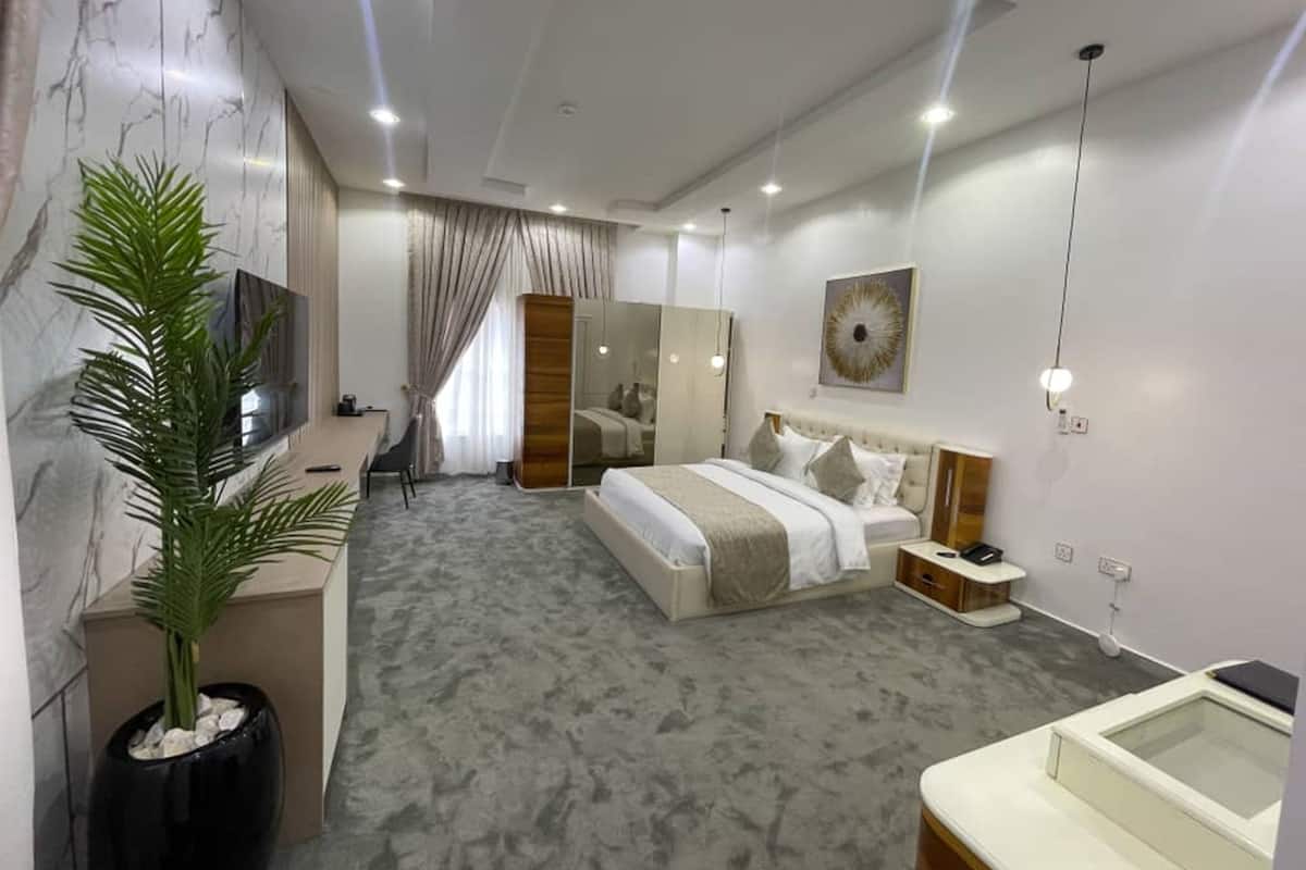 A modern hotel room with a large bed, a desk, a mirror, and a potted plant.