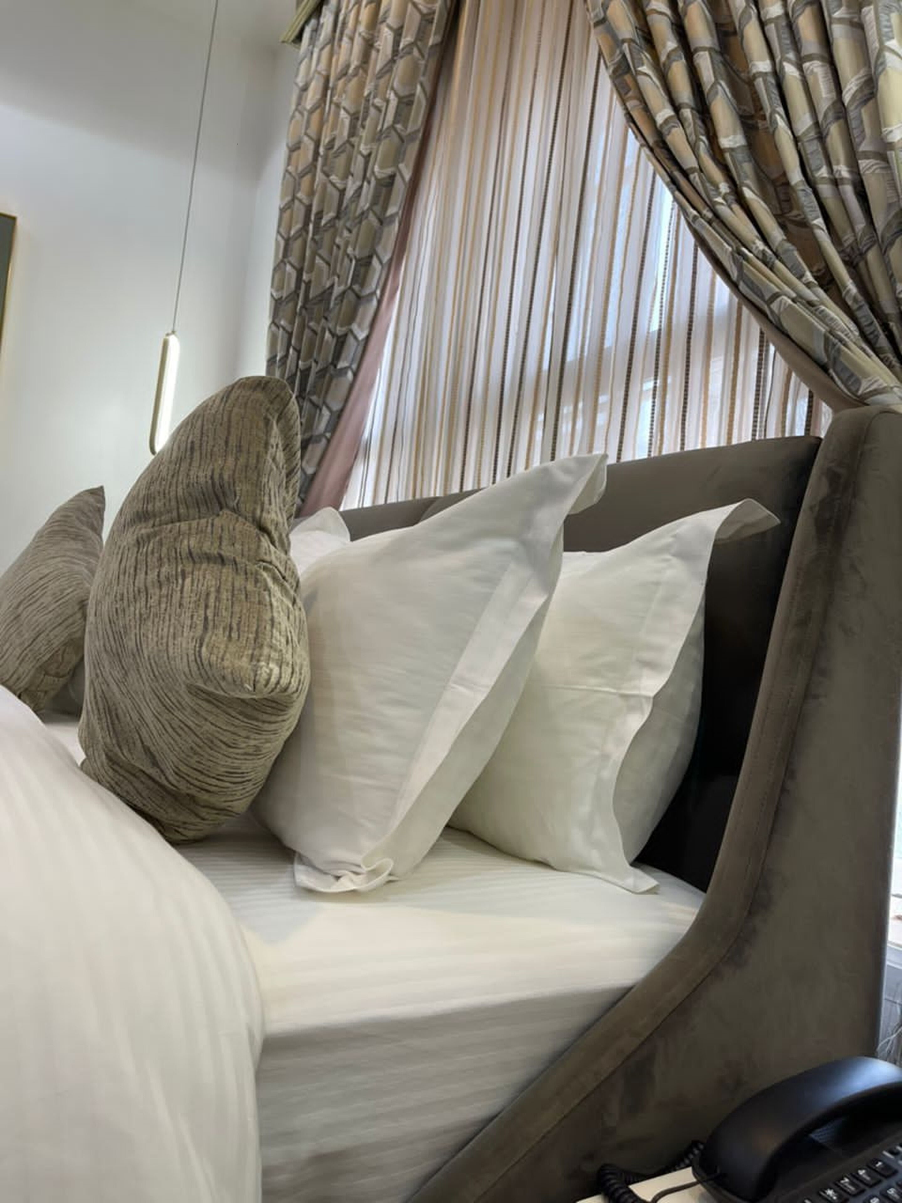 Un lit avec du linge de lit blanc, une tête de lit marron foncé et plusieurs oreillers, dont un avec une texture particulière.