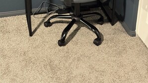A corner office chair with a mesh backrest, attached to a black metal desk with a cable connected to a power outlet.