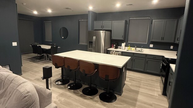 A modern kitchen with grey cabinets, a stainless steel refrigerator, and a bar area with stools.