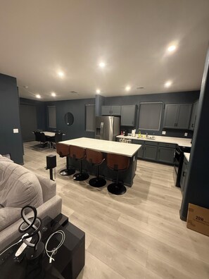 Een moderne keuken met grijze kastjes, een roestvrijstalen koelkast en een bar met krukken.