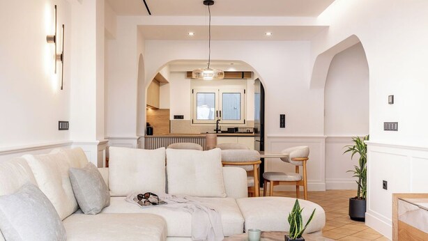 Un salon moderne avec un canapé d’angle, une table basse et une vue sur la cuisine grâce à une arche.