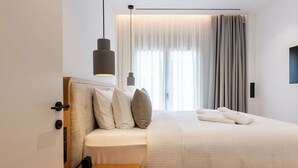 Une chambre d’hôtel moderne avec un lit bien fait, une table de chevet, un luminaire suspendu et une grande fenêtre avec des rideaux.