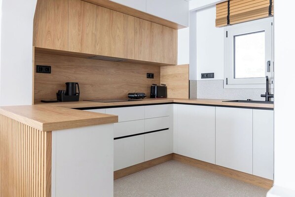 Una cocina moderna con armarios blancos, encimera de madera y una ventana con persianas.