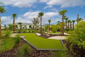 A golf course with a putting green, palm trees, and a building in the background. - 16109 Castaway at Windsor Cay: 5BR Pool Townhome (Clermont)