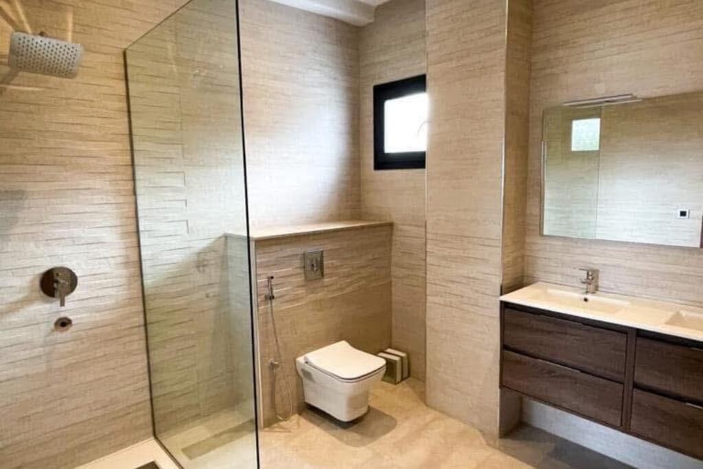 Une salle de bain moderne dotée d’une douche à parois de verre, de toilettes et d’un meuble-lavabo avec un miroir.
