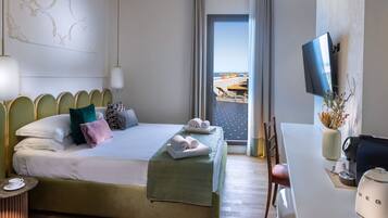 Habitación de hotel con cama, escritorio con cafetera, televisión y vista a la playa.