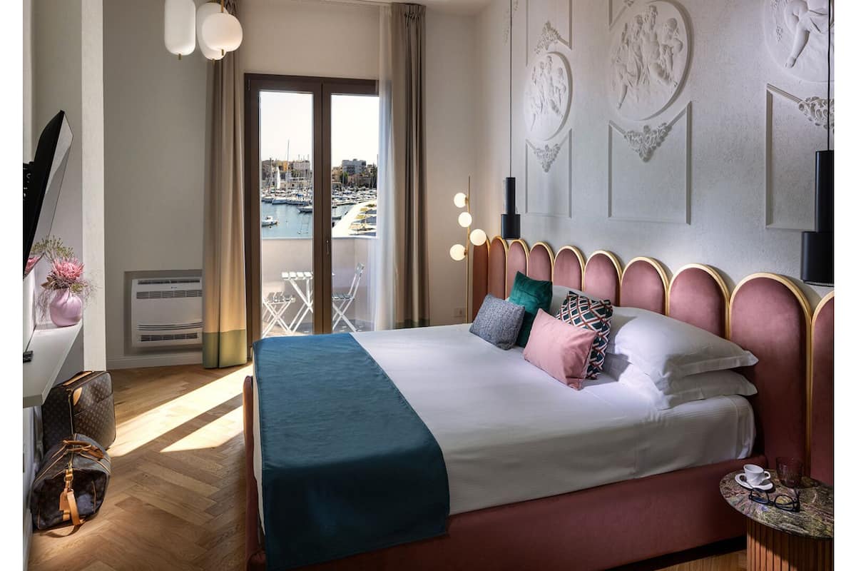 Une chambre d’hôtel avec un lit, une vue sur le port de plaisance et un balcon équipé d’une table et de chaises.