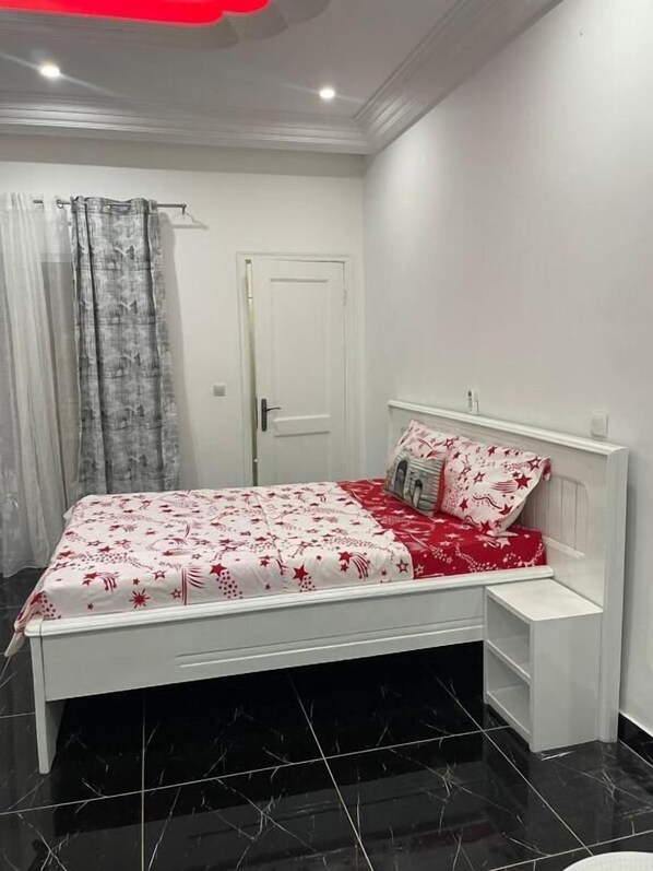 Une chambre à coucher avec un lit, une table de chevet, une porte et un rideau.