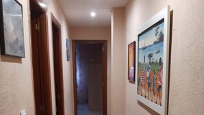 A hallway with beige walls, a tiled floor, and wooden doors. There are framed pictures on the walls.