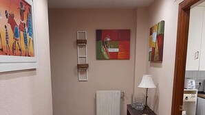 A hallway with a tiled floor, a radiator, a small table with a lamp, and a painting on the wall.