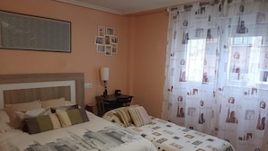 A hotel room with a large bed, a bedside table, a lamp, and a window with curtains.
