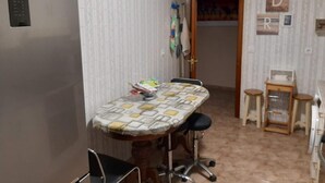 A compact kitchen with a refrigerator, a table with a patterned tablecloth, and a chair.