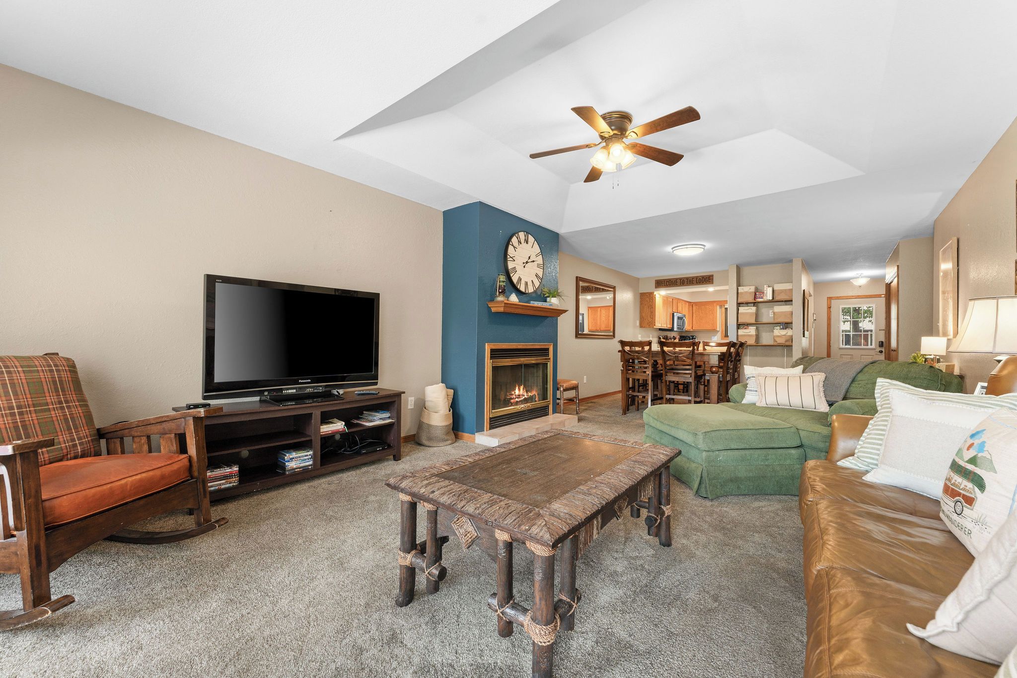 A living room with a television, a fireplace, a ceiling fan, and a dining area.