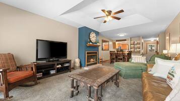 A living room with a television, a fireplace, a ceiling fan, and a dining area.