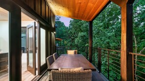 Une terrasse en bois avec une table et des chaises, entourée de portes vitrées et d’une rambarde en métal.