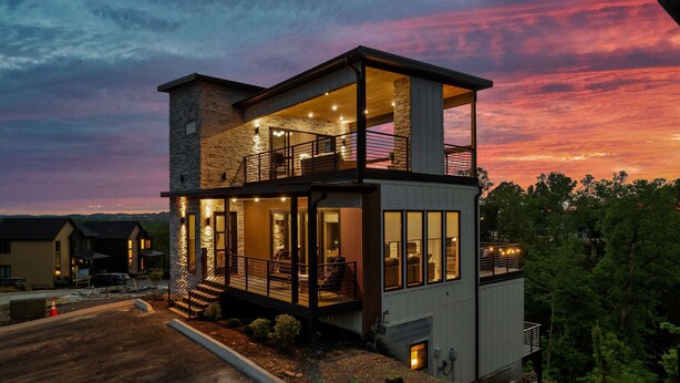 A modern two-story house with a balcony, large windows, and a stone facade.