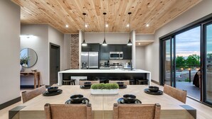 A modern kitchen with a central island, wooden ceiling, and large windows.