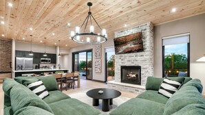 A modern living room with a green sectional sofa, a fireplace, and a dining area with a kitchen in the background.