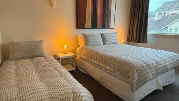 Habitación de hotel con dos camas, una mesita de noche, un cuadro en la pared y una ventana con cortinas.