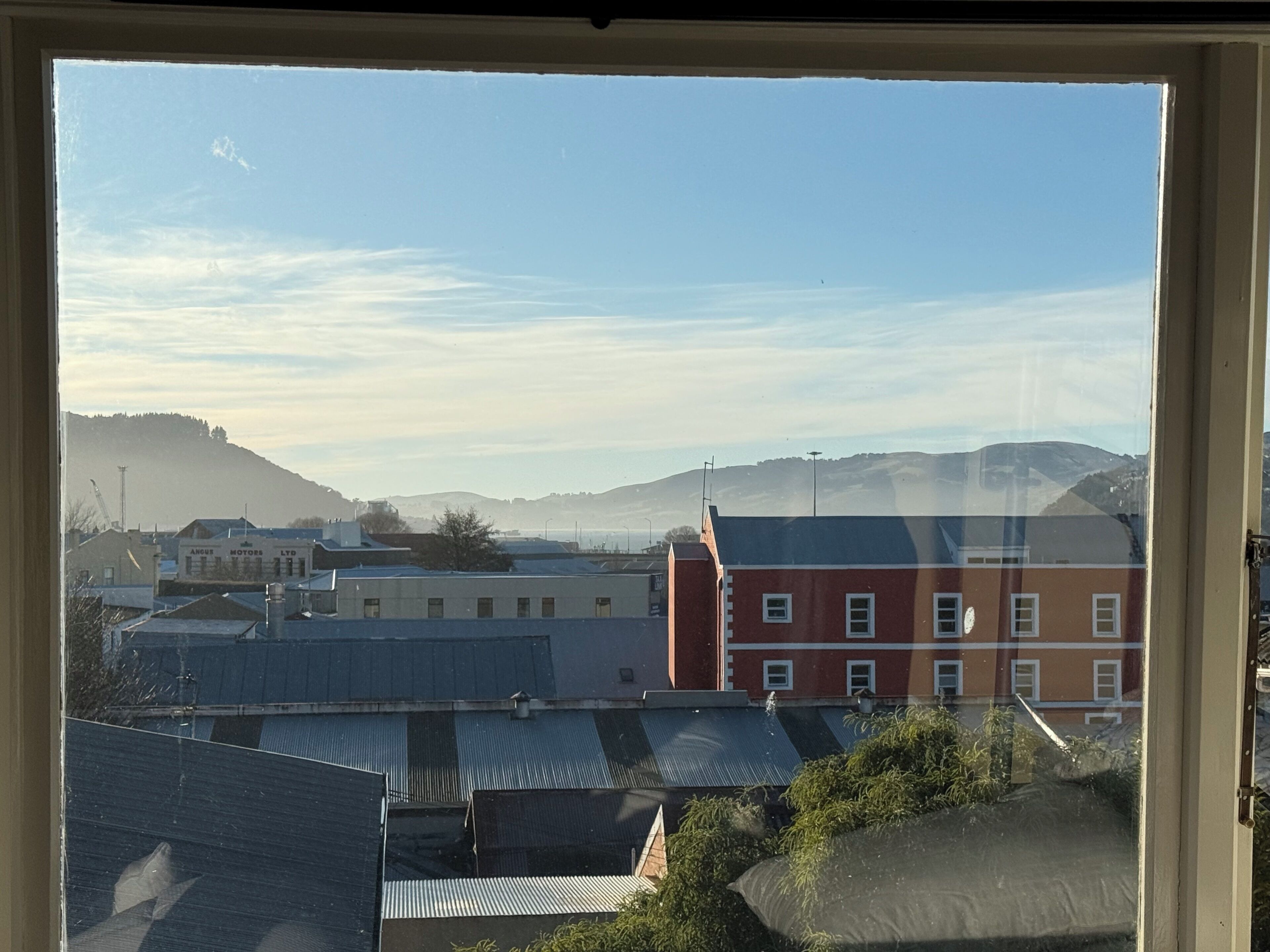 A view through a window of a building with a red facade, a blue roof, and a mountainous background.